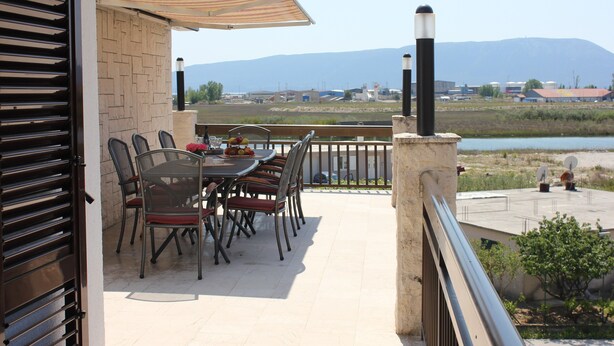 Eine Terrasse mit Tisch und Stühlen, Blick auf ein Gewässer und Berge in der Ferne.