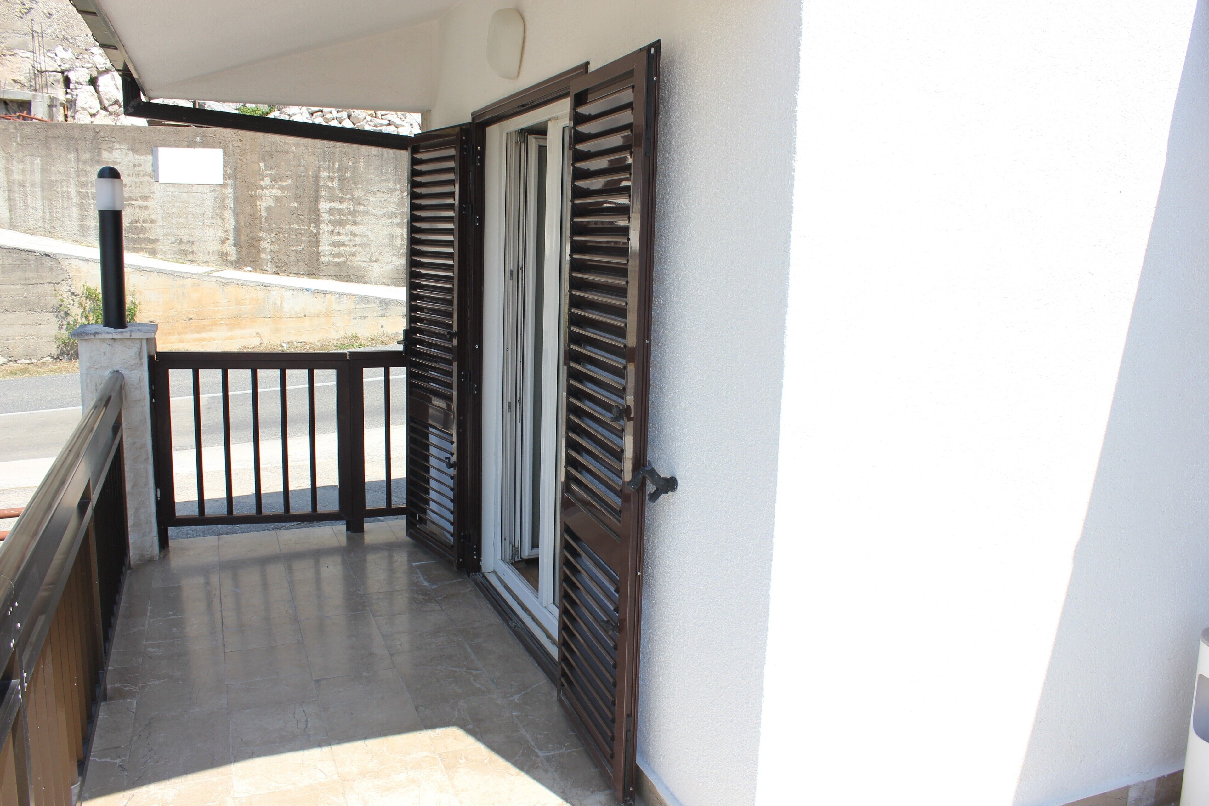 A balcony with a metal railing, a door with a window, and a concrete wall in the background.