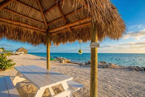 A beach with a thatched-roof structure, a sign reading 'Jolly's Beach,' and a picnic table. - Scenic Oceanview Haven Pool Beach Access U7 (Marathon)