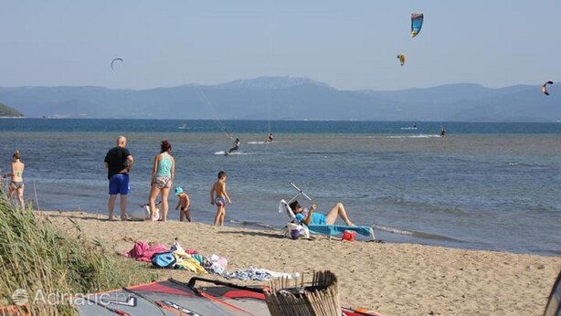 Une plage où l’on voit des gens, des cerfs-volants et des bateaux.