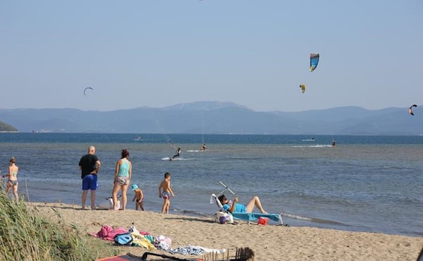 A beach with people, kites, and boats.