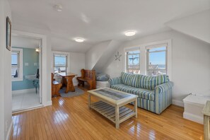 Un salón amplio con suelo de madera, un sofá a rayas, una mesa de centro y un comedor con mesa y sillas de madera.