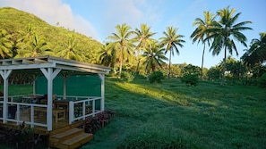 A wooden structure with a green roof, possibly a guesthouse or a small pavilion, surrounded by lush greenery and palm trees. - Charming Farm Cottage "Hibiscus" Breakfast & Bikes  (Matavera)