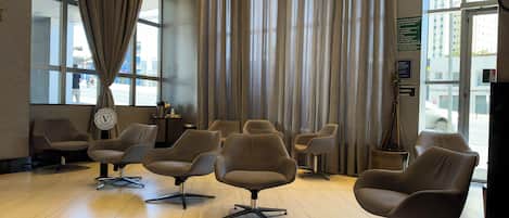A hotel lobby with modern chairs, a reception desk, and large windows with curtains.