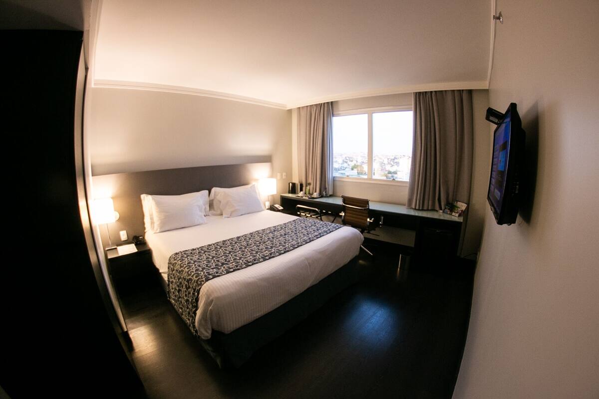 A hotel room with a bed, desk, chair, and a TV mounted on the wall.