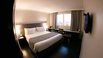 Habitación de hotel con cama, escritorio, silla y televisor montado en la pared.