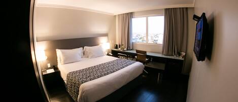A hotel room with a bed, desk, chair, and a TV mounted on the wall.