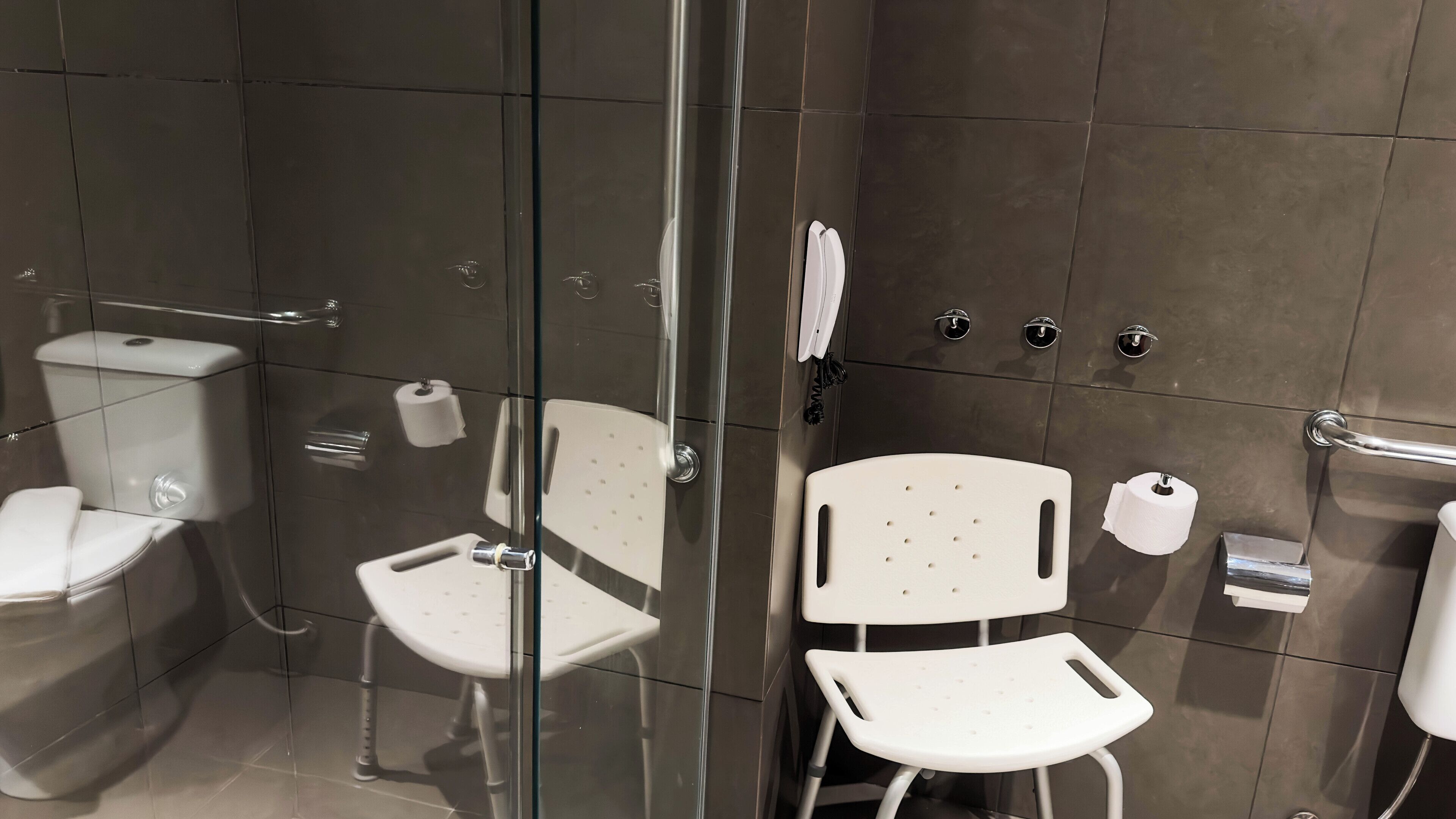 Un baño moderno con cabina de ducha de vidrio, inodoro, bidé y una silla blanca.