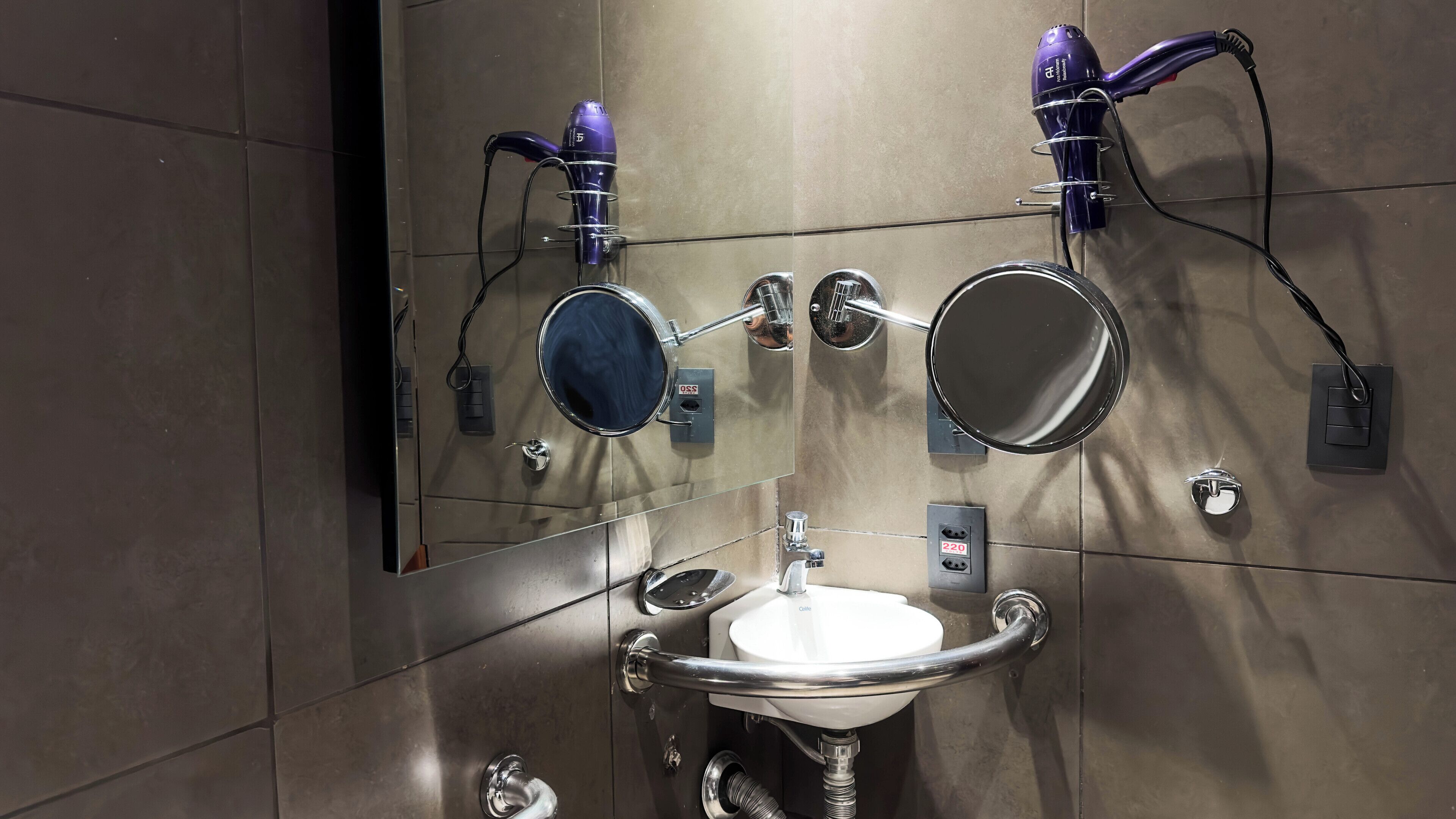 A modern bathroom with a large mirror, two hair dryers, a sink, and a towel rack.