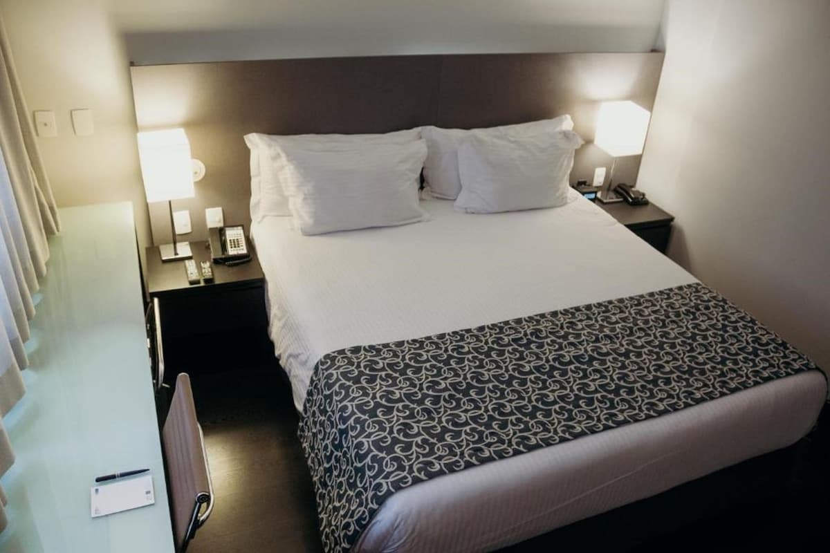 A hotel room with a bed, two bedside tables, a lamp, and a telephone.