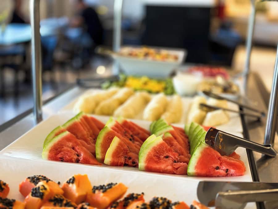 Un bufé con diversas frutas y verduras, incluyendo rebanadas de sandía y trozos de papaya.