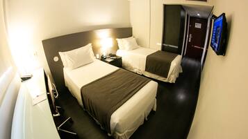 Quarto de hotel com duas camas, uma escrivaninha, uma cadeira, uma televisão e uma porta.