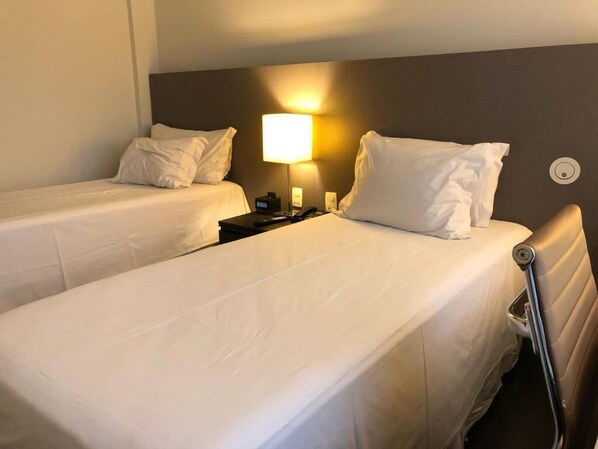 A hotel room with two single beds, a nightstand, a lamp, and a wall-mounted radiator. - Gran Vivenzo Cidade Nova (Belo Horizonte)