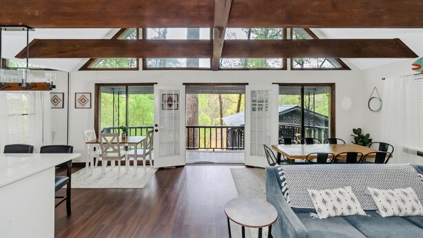 Un interior espacioso con techo alto, vigas de madera, un comedor, un sofá y ventanas amplias que ofrecen vistas al exterior.