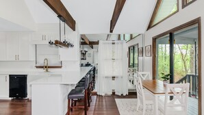 Una cocina moderna con armarios blancos, una isla de madera y un comedor con sillas blancas.