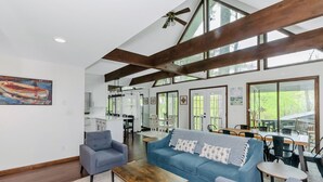 Un salón espacioso con techos altos, vigas de madera a la vista, un sofá azul, una mesa de centro y un área de comedor con sillas y una mesa.