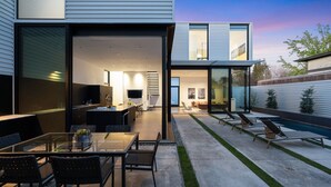Ett modernt hus med ett öppet kök och matplats, en pool och en uteplats med bekväma loungestolar.