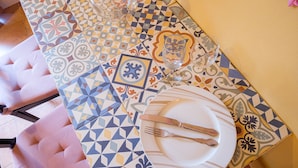 A dining table with a colorful geometric tile pattern, a white plate with a fork and knife, and a glass. - Y.Quebedo - Boutique Apartments - Poetico (Setúbal)