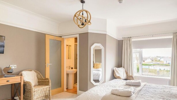 Un dormitorio con cama, escritorio, silla, espejo y ventana con vistas.