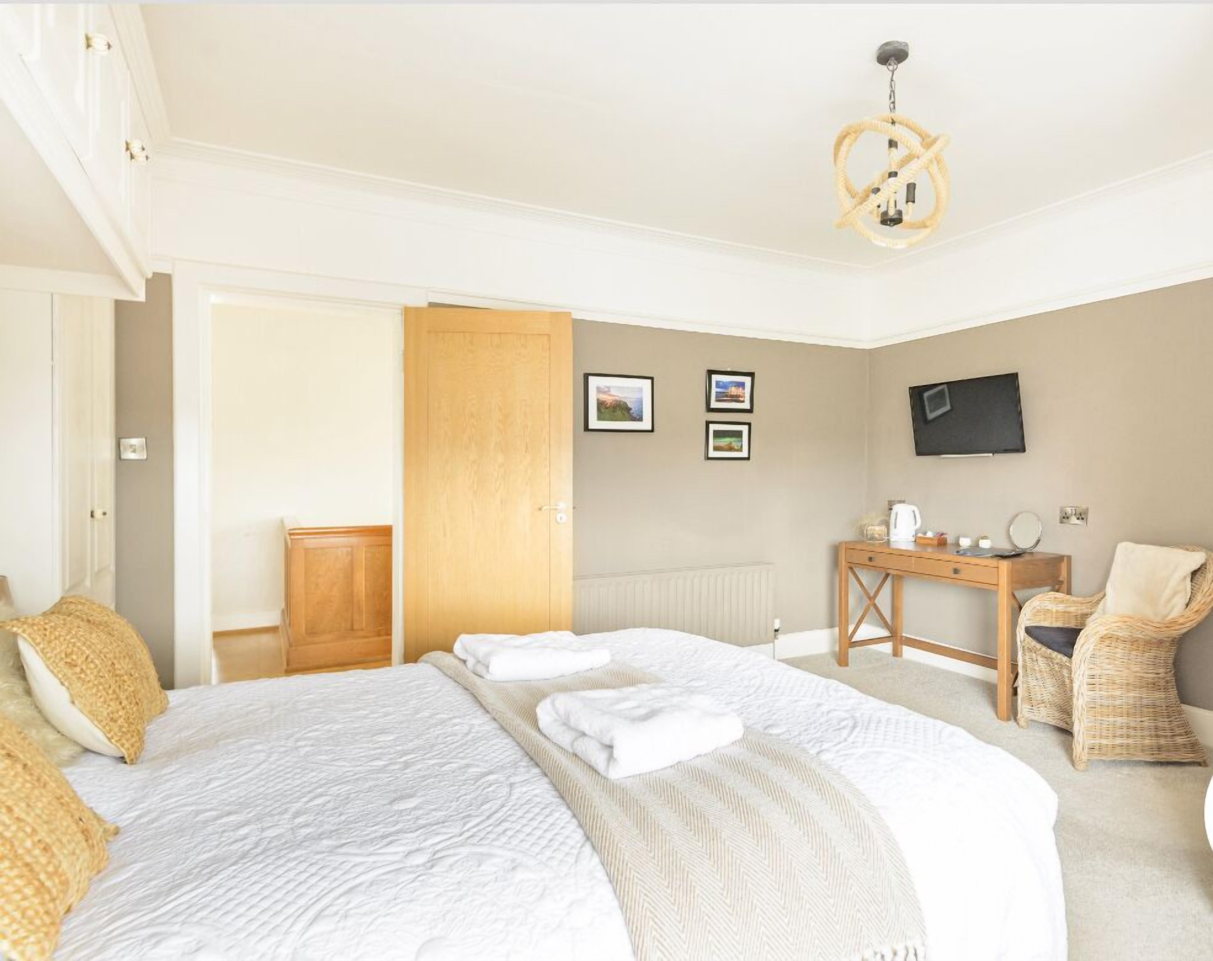 A hotel room with a large bed, a wooden desk, a chair, a television, and a door leading to another room.