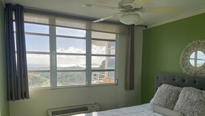 A bedroom with a bed, a ceiling fan, a window with curtains, a wall-mounted air conditioner, and a round mirror. - Apartment with ocean view near Ceiba FerryTerminal (Ceiba)