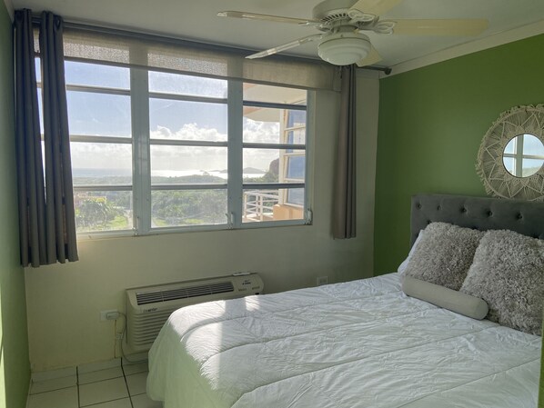 A bedroom with a bed, a ceiling fan, a window with curtains, a wall-mounted air conditioner, and a round mirror. - Apartment with ocean view near Ceiba FerryTerminal (Ceiba)