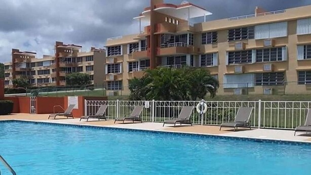 Une piscine avec des chaises longues et, au fond, un bâtiment doté de nombreux balcons.