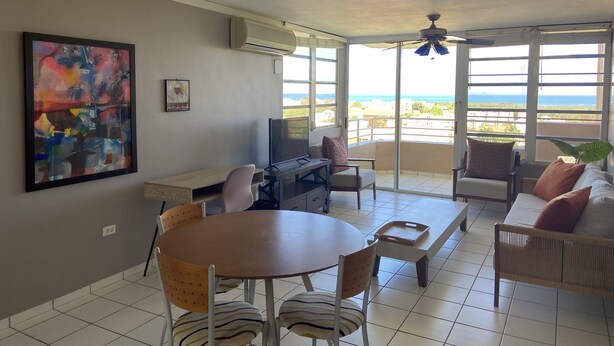 A spacious living area with a dining table, chairs, a sofa, and a large window offering a view of the ocean. - Apartment with ocean view near Ceiba FerryTerminal (Ceiba)