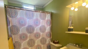 Une salle de bain avec un rideau de douche à motifs, des toilettes, un lavabo et un miroir avec des lumières au-dessus.