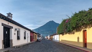 Una calle adoquinada flanqueada por edificios, con una montaña al fondo y un coche estacionado al costado.