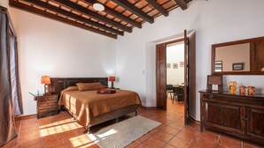 Un dormitorio con cama, cabecera de madera, mesita de noche con lámpara, cómoda y espejo.