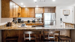 Una cocina con armarios de madera, encimeras de granito, un refrigerador de acero inoxidable y asientos de bar.
