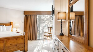 Una habitación de hotel con una cama de madera, un aparador, una silla y un espejo grande.