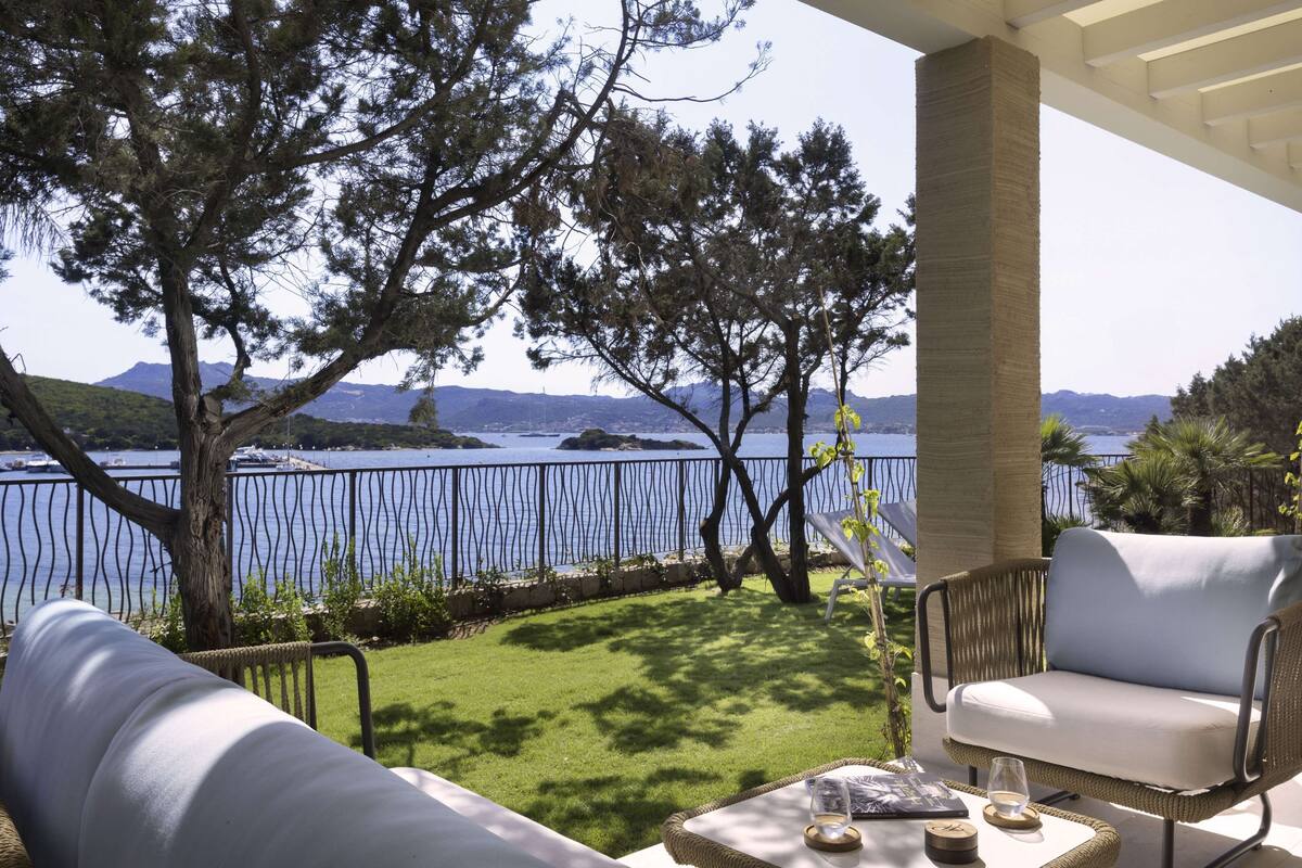 Une terrasse offrant une vue sur la mer et les montagnes, aménagée avec des meubles en osier et une table en verre.