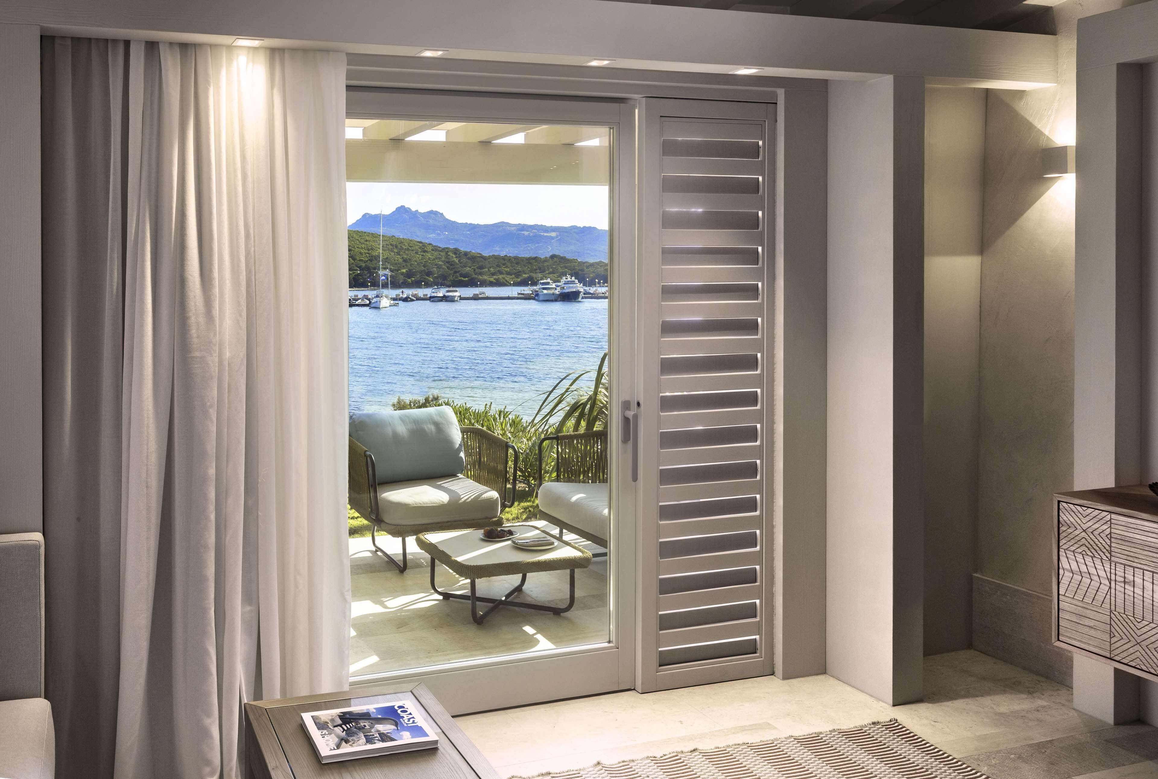 Quarto com porta de correr de vidro que dá para uma varanda com vista para o mar e barcos.