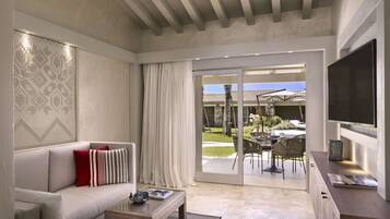 Una sala de estar moderna con un sofá, una mesa de centro y un televisor. Hay un ventanal corredero que da a un patio al aire libre con una mesa y sillas de comedor.