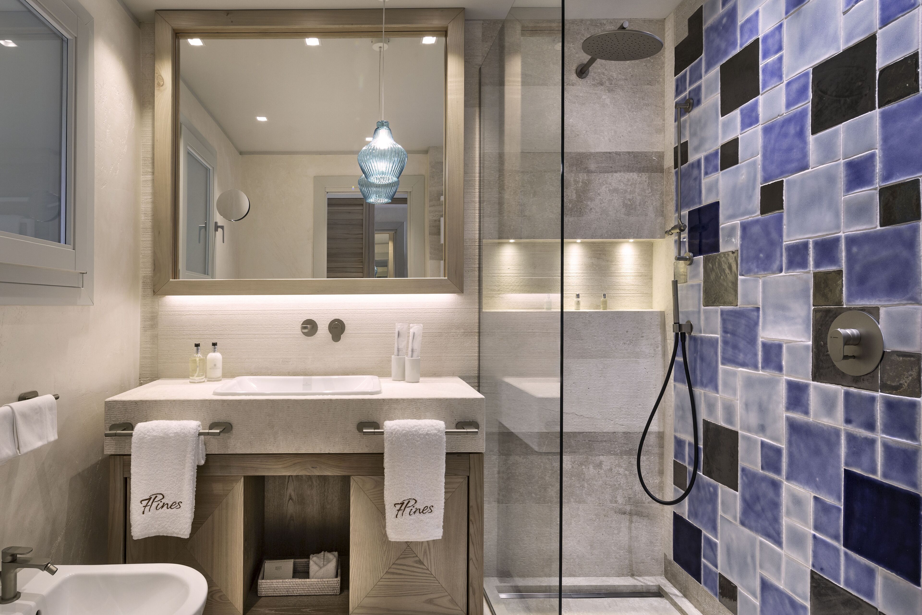 A modern bathroom with a large mirror, two sinks, a shower, and a towel rack with towels.