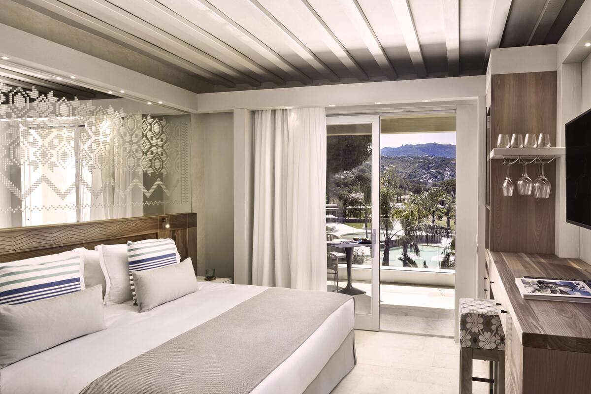 Une chambre d’hôtel moderne dotée d’un grand lit, d’une télévision, d’un bureau en bois et d’un balcon avec vue sur la piscine.