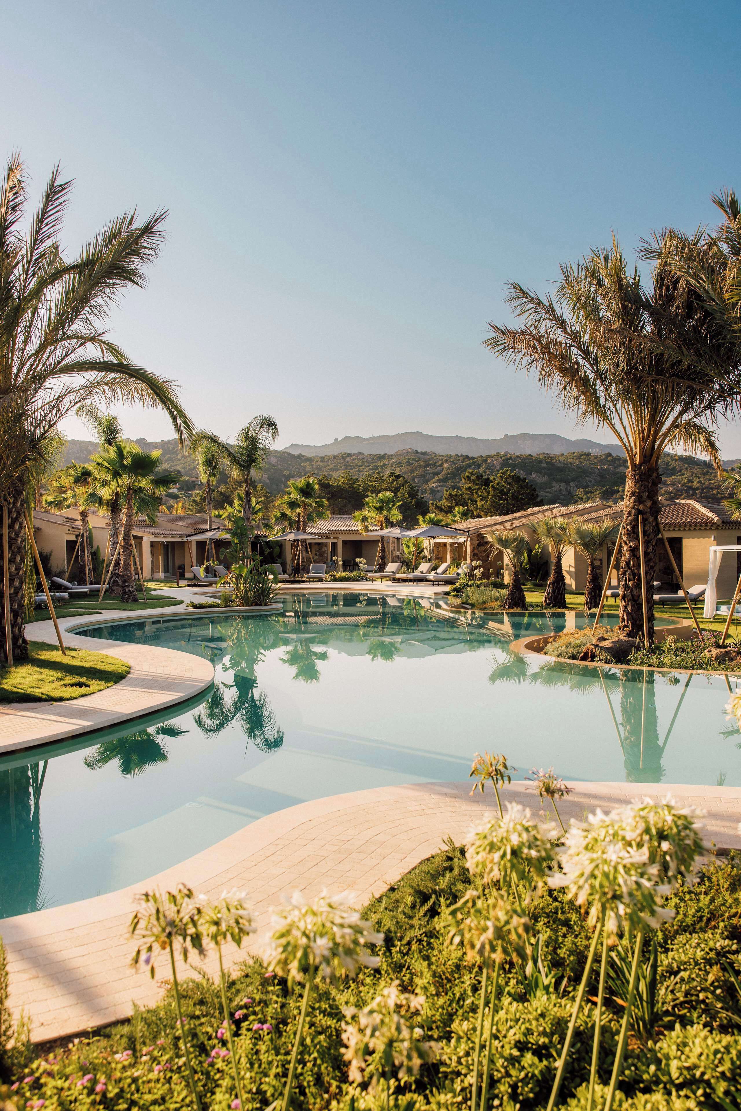 A resort with a large swimming pool surrounded by palm trees and lounge chairs.