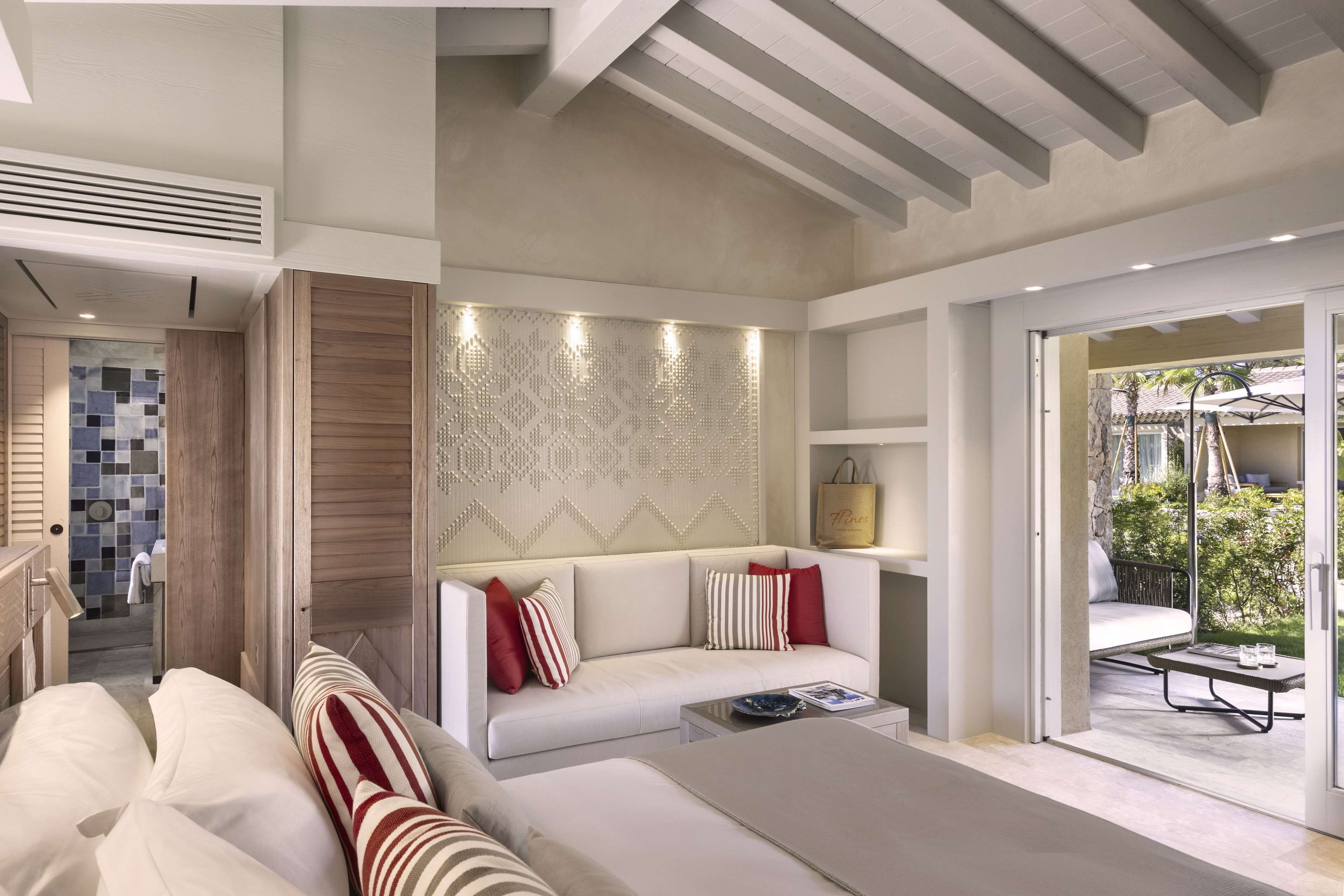 A modern living room with a sofa, a coffee table, and a patterned wall. There is a door leading to a balcony with outdoor furniture.