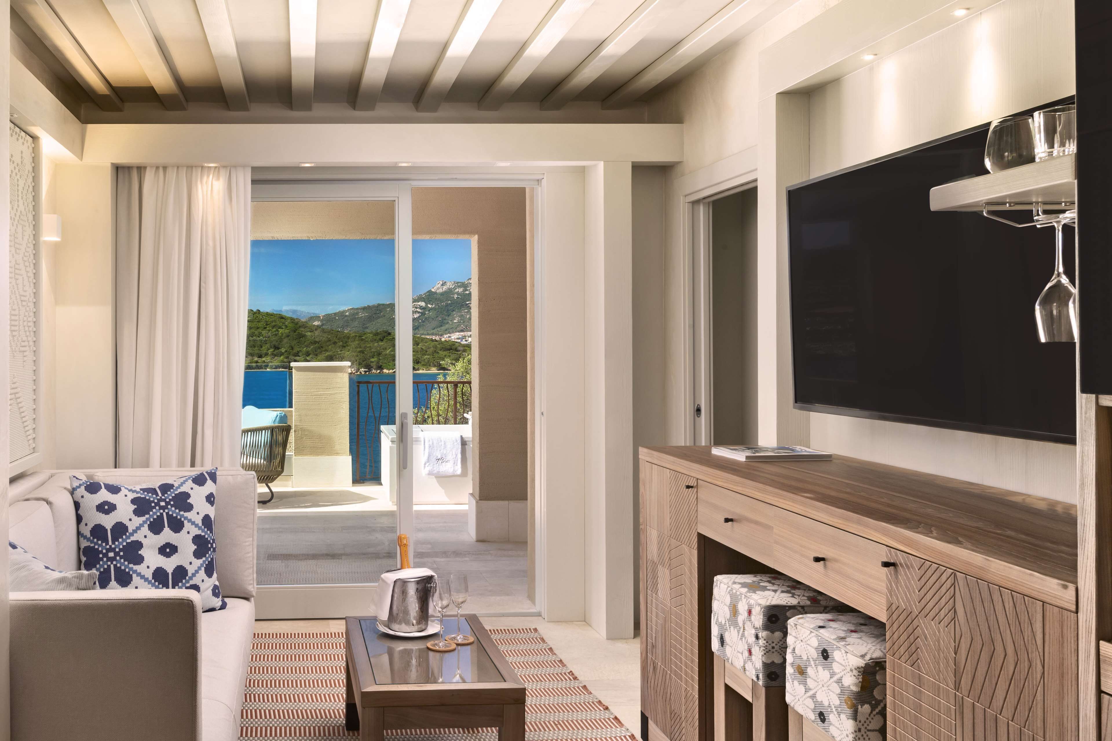 Un salon moderne avec un canapé, une table basse, un téléviseur et une vue sur un balcon équipé d’une table et de chaises.