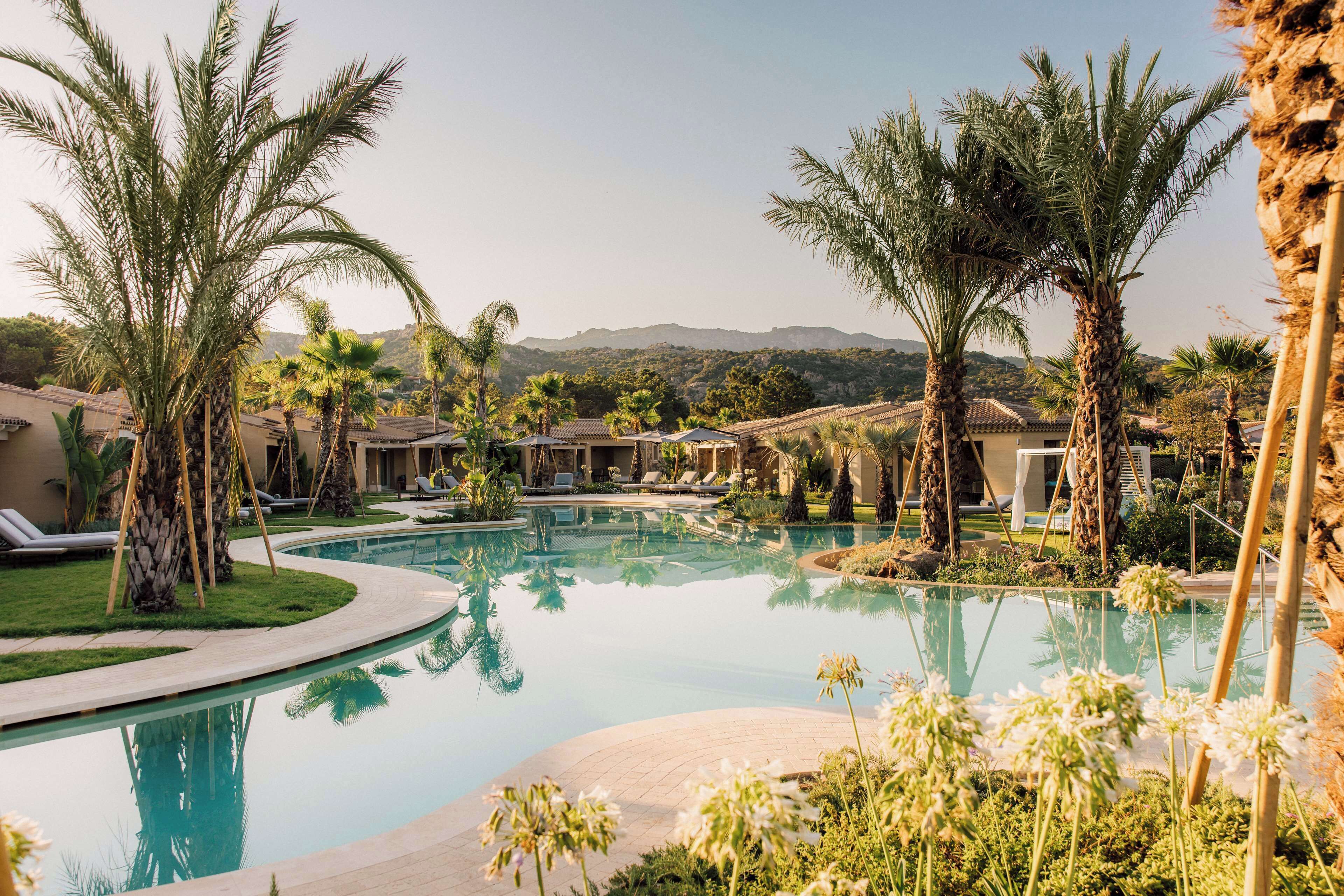 Un resort con piscina, palmeras y vistas a colinas distantes.