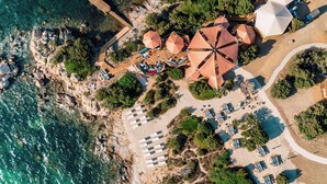 Vue aérienne d’une station balnéaire avec des parasols, des chaises longues et une terrasse en bois donnant sur la mer.