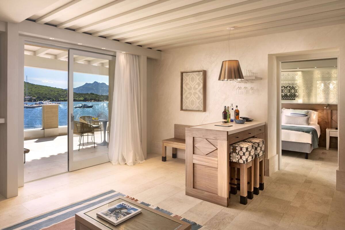 Une chambre d’hôtel moderne avec balcon, un bureau en bois, un lit et vue sur la mer.