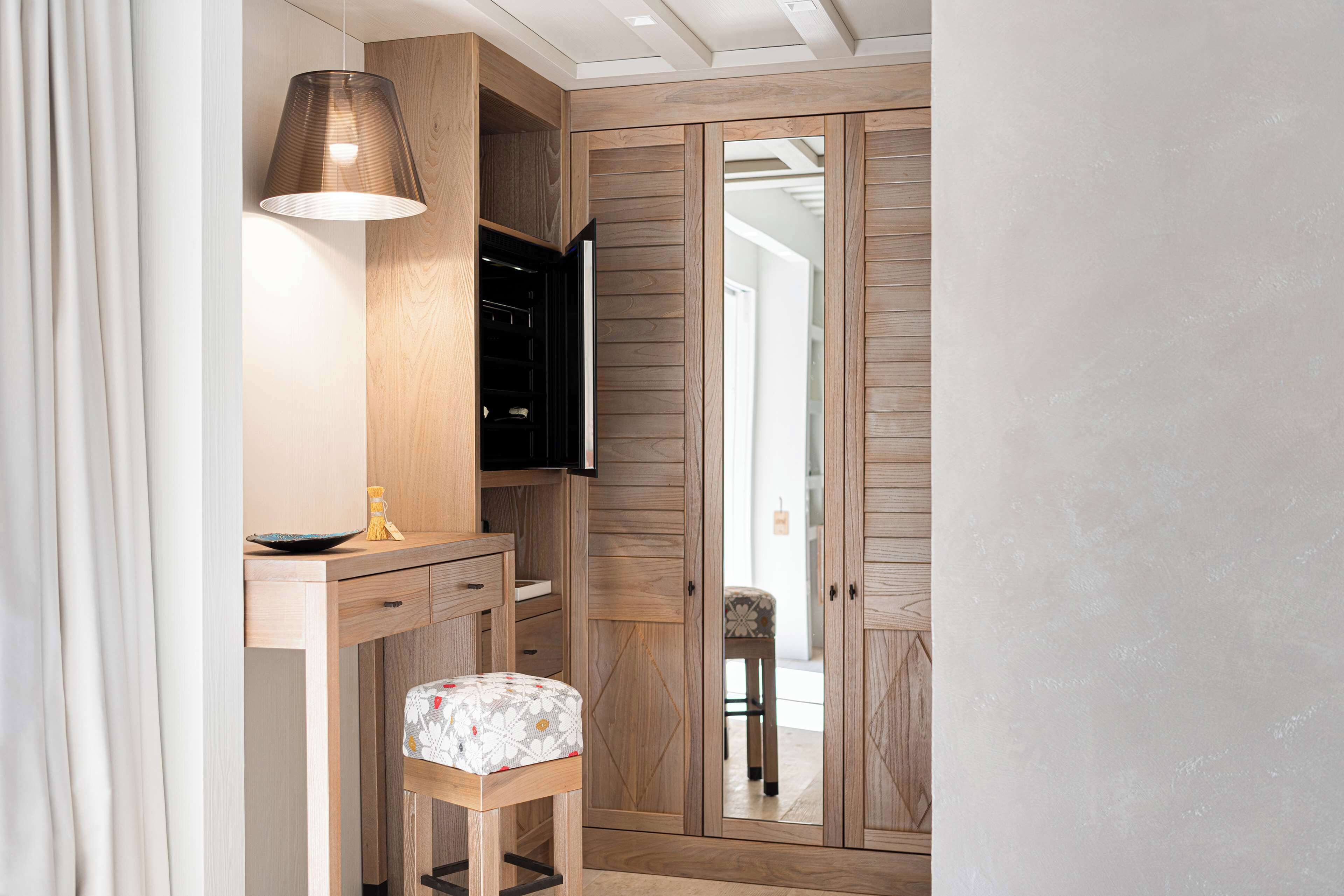 A modern room with a wooden wardrobe, a desk with a lamp, and a chair.