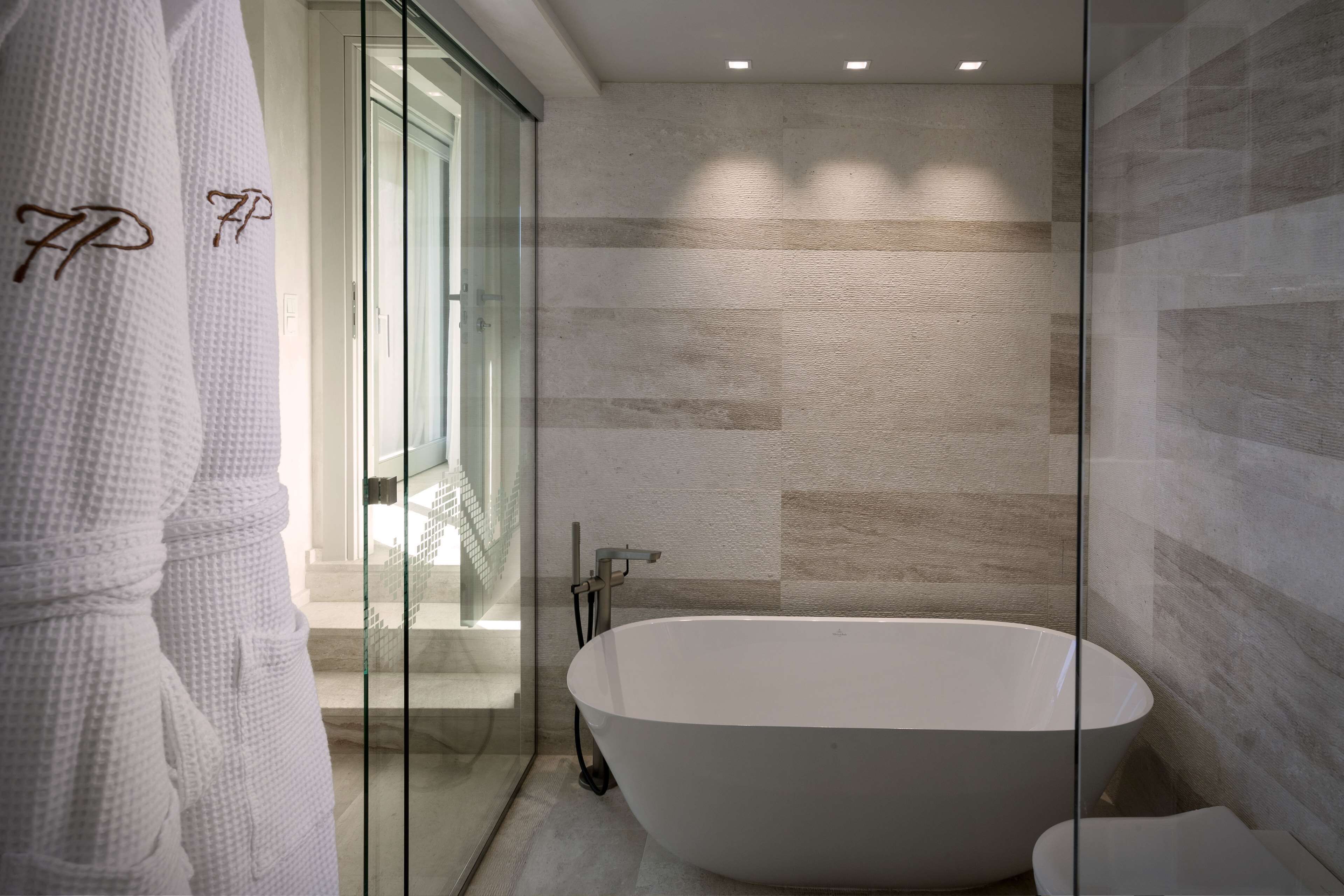 Un baño moderno con bañera independiente, cabina de ducha con mampara de vidrio y puerta de cristal que da a una escalera.