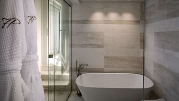 Un baño moderno con bañera independiente, cabina de ducha con mampara de vidrio y puerta de cristal que da a una escalera.
