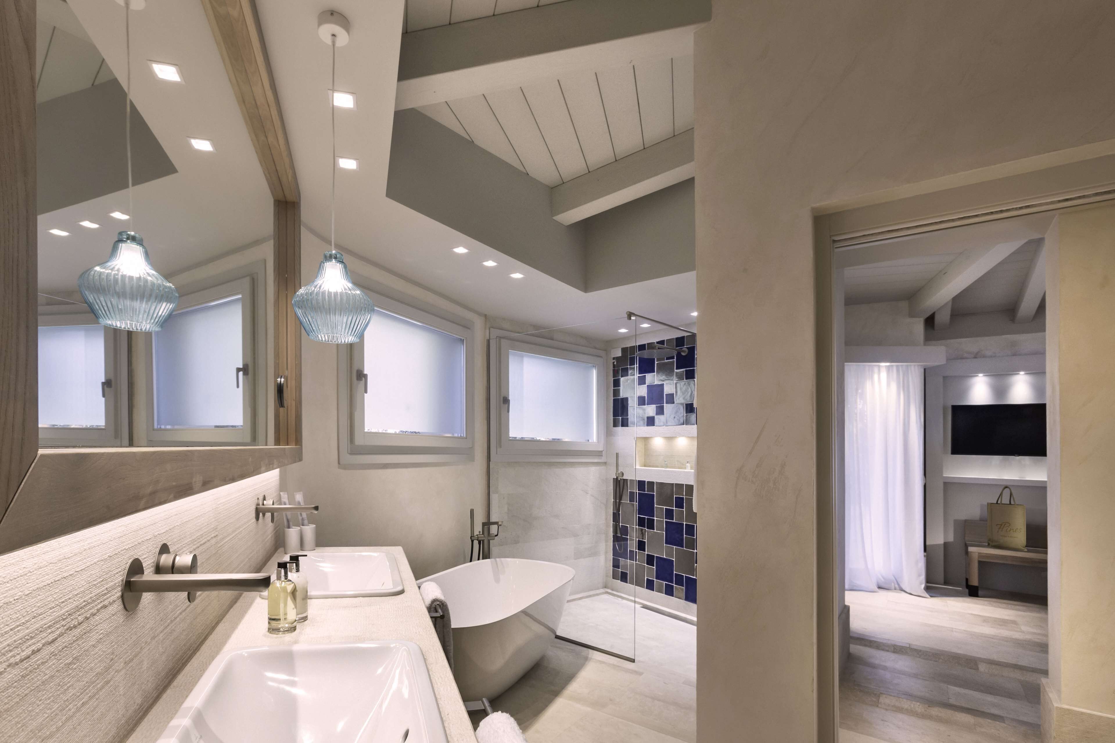 A modern bathroom with a freestanding bathtub, a large mirror, and pendant lighting.
