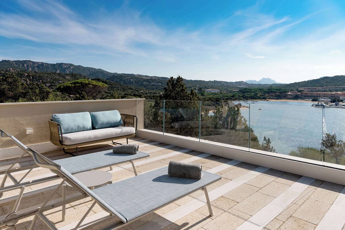 Une terrasse dotée d’un canapé et de fauteuils, offrant une vue panoramique sur les montagnes et un plan d’eau.
