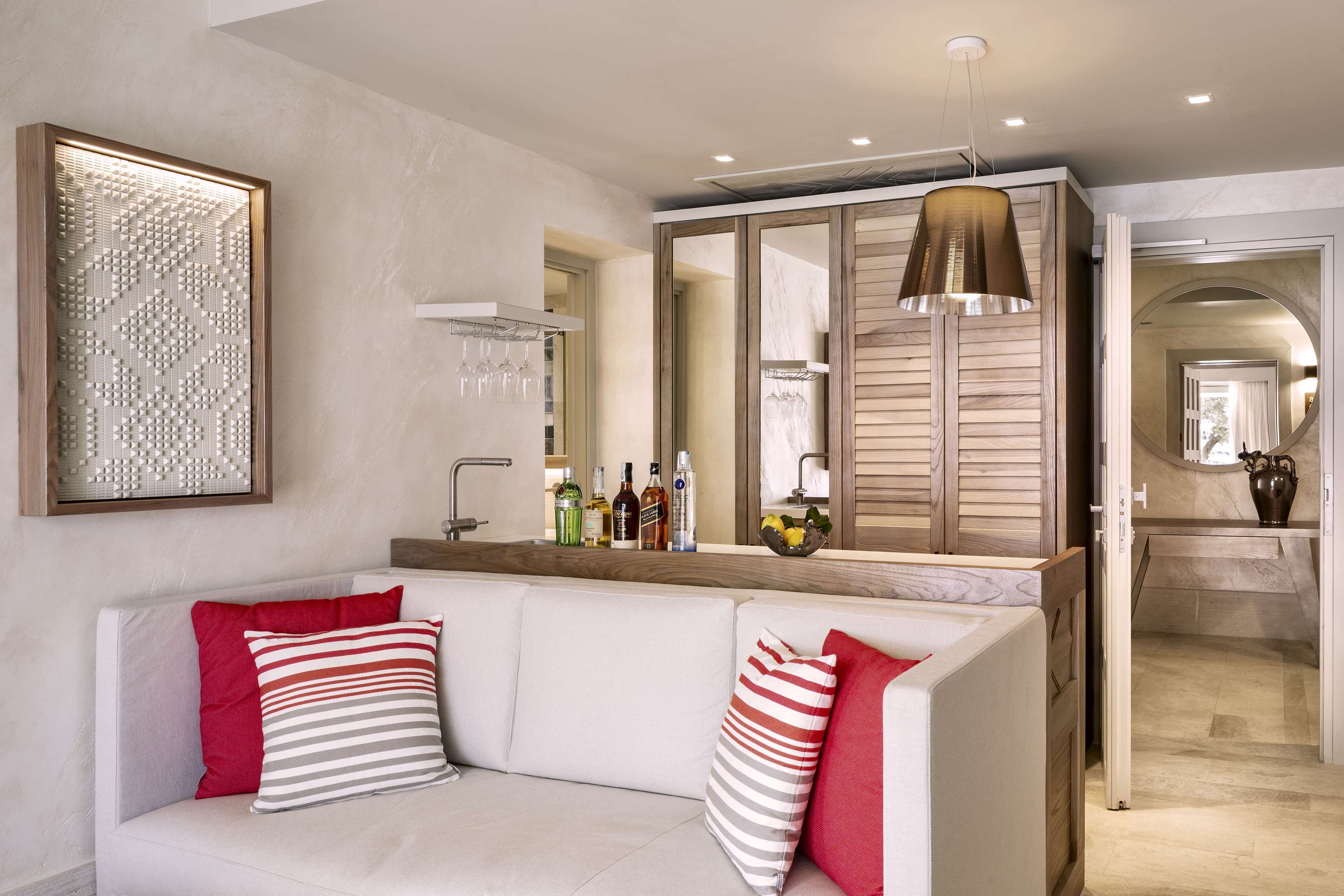 A modern living room with a white sofa, red and striped pillows, a wooden sideboard with a mirror, and a hanging pendant light.